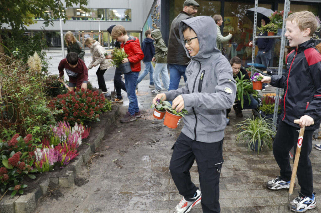 Leerlingen van De Achtbaan dragen planten naar de nieuwe border op het schoolplein