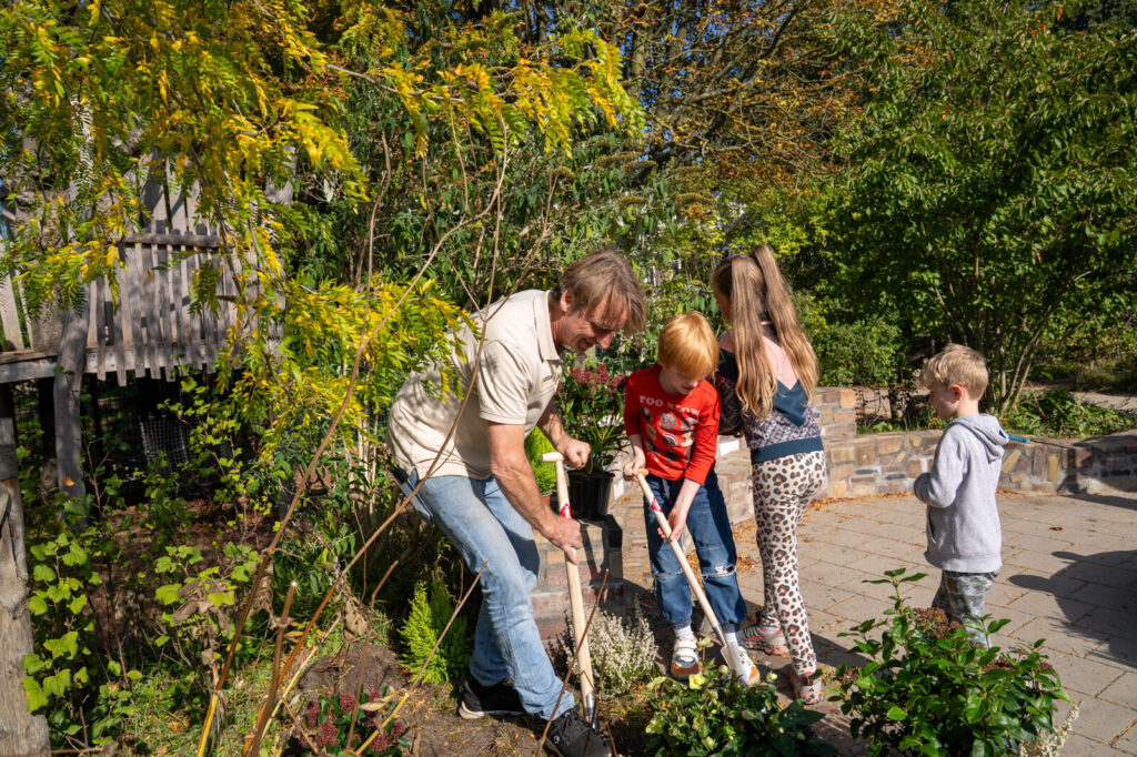 Leerlingen graven samen met hun begeleider een plantgat in de border